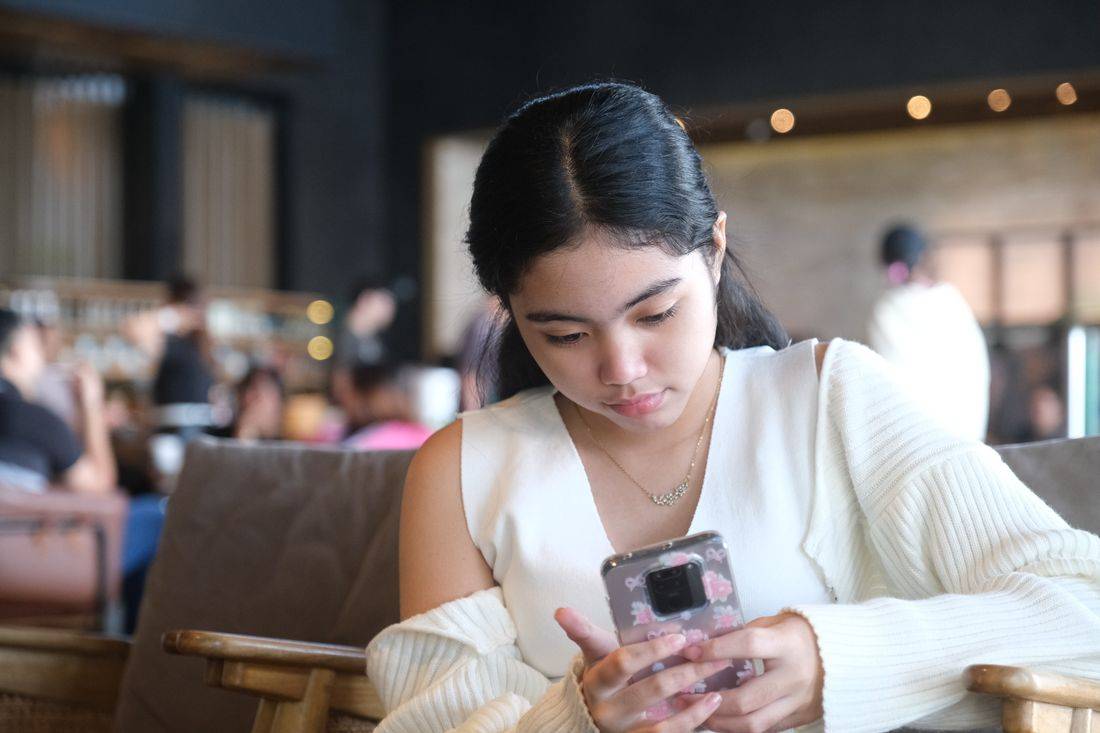 Pembaca menikmati artikel Surga5000 dari ponsel di kedai kopi